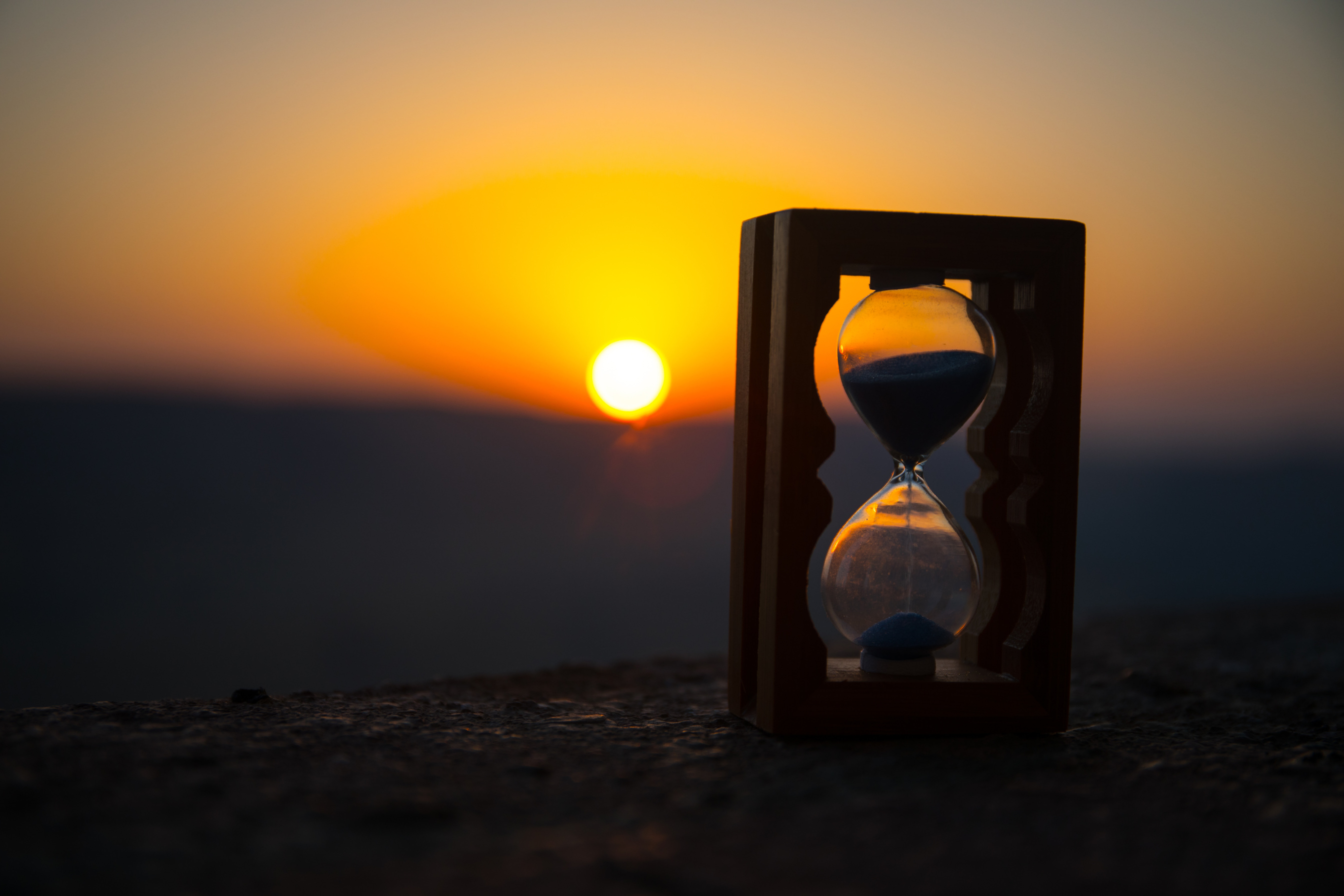 Hourglass Passing of Time Lapse Clouds. An hourglass in front of a bright blue sky with puffy white clouds passing. Time concept. Sunset time